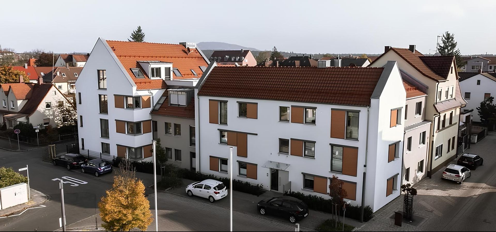 Ansicht eines modernen Wohngebäudes mit roten Dächern und grünen Bäumen.